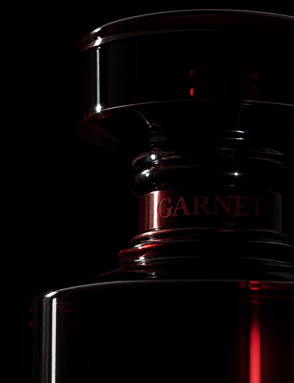 Macro detail of a dark glass perfume bottle neck with a garnet highlight